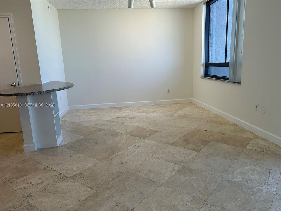 Large format stone tile flooring, built-in peninsula with a curved surface, and a single vertical window with dark framing