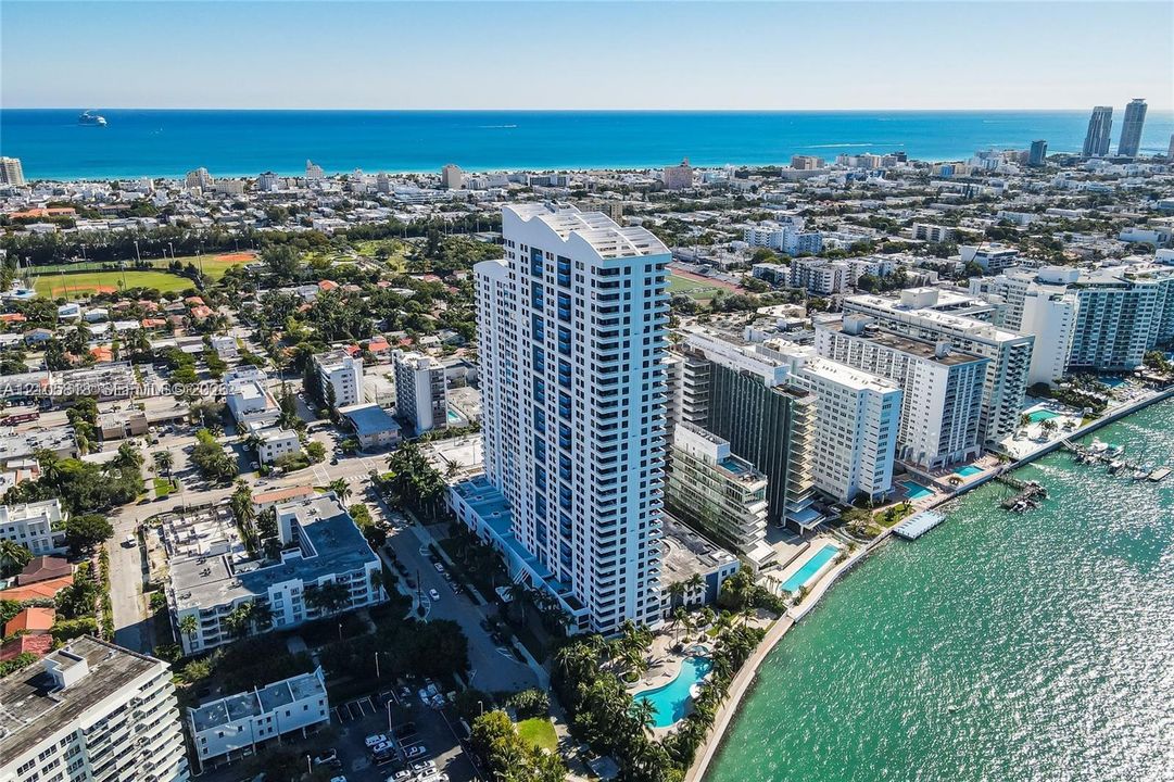 High-rise residential tower featuring a swimming pool, waterfront positioning, multiple balconies, and proximity to the coastline