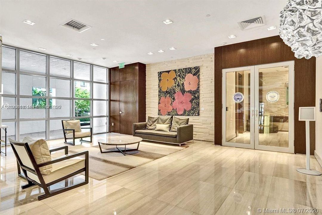 Lobby interior featuring expansive floor-to-ceiling windows, polished stone flooring, recessed ceiling lighting, a stacked stone accent wall, and wood-paneled door surrounds