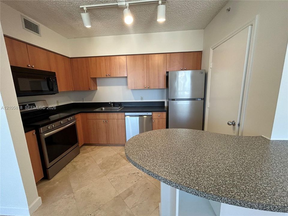 Kitchen featuring wood-finish cabinetry, stainless steel appliances, stone-texture countertops, tile flooring, and track lighting