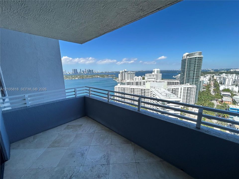 Covered balcony featuring stone tile flooring and white metal railings with water and skyline scenery