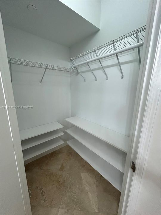 Storage space featuring white tiered shelving, wire rack organizers, and tile flooring