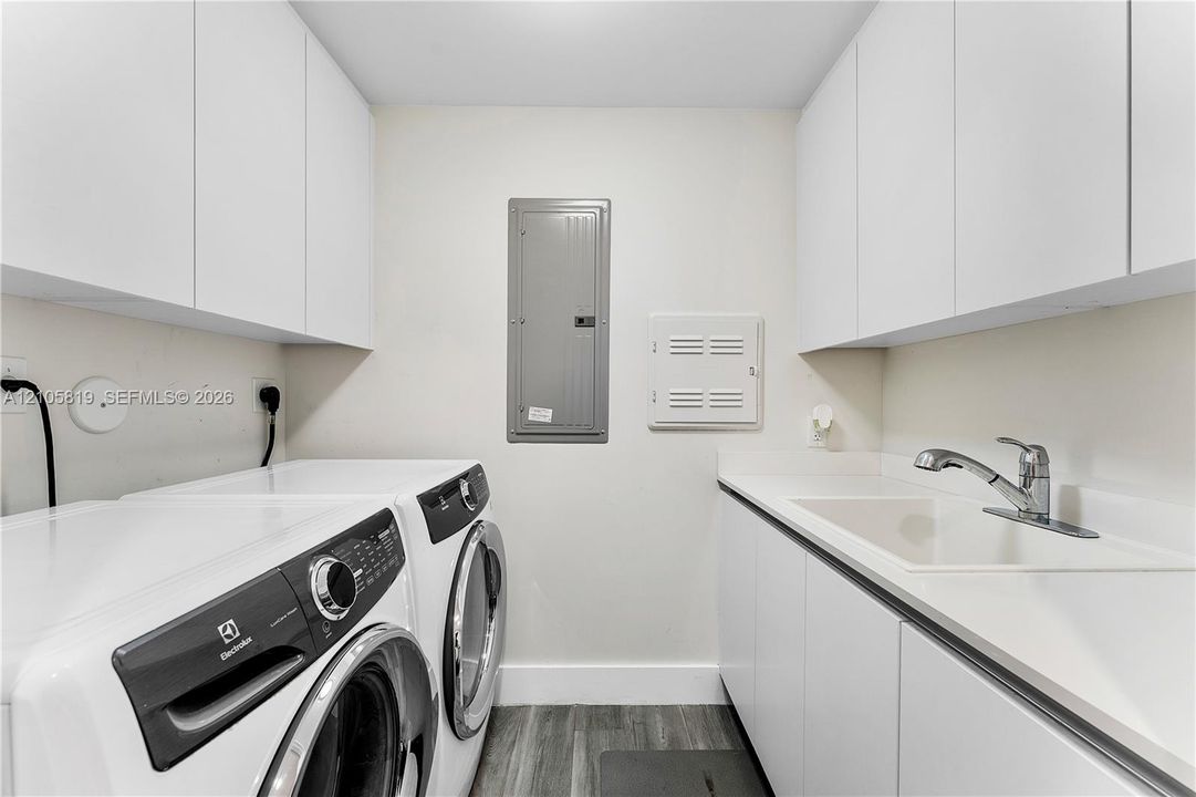Laundry area featuring white cabinetry, integrated sink with chrome faucet, and wood-finish flooring