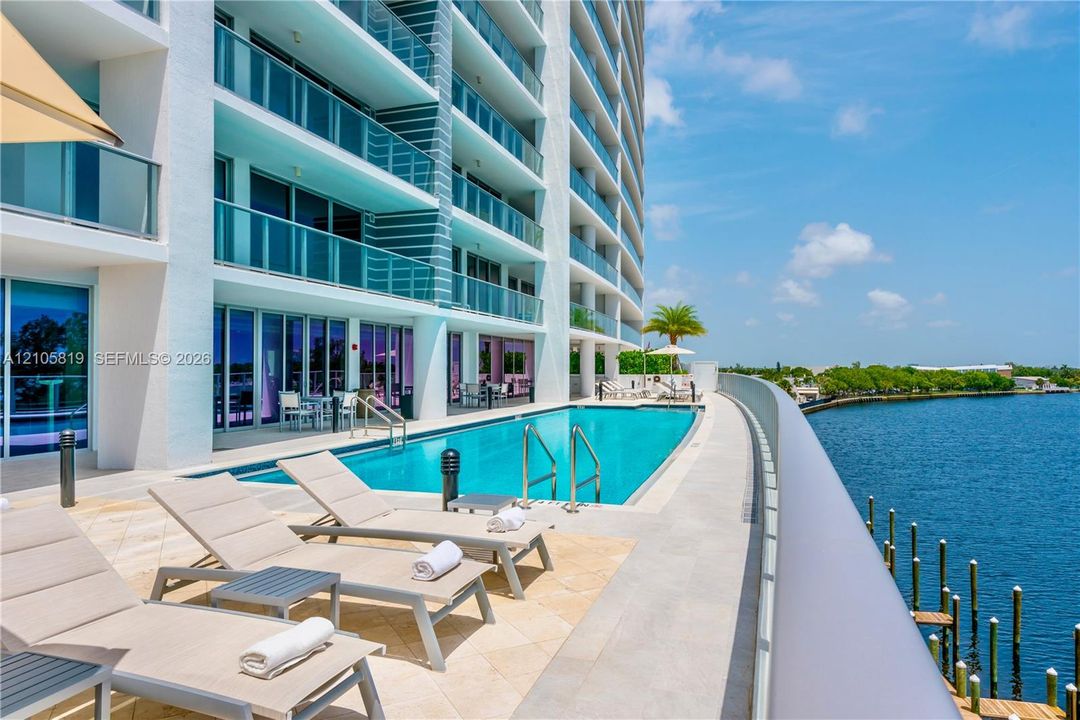 Heated Pool Overlooking Middle River.  Waterfront terrace featuring a rectangular swimming pool, stone-tile decking, and glass-railing balconies