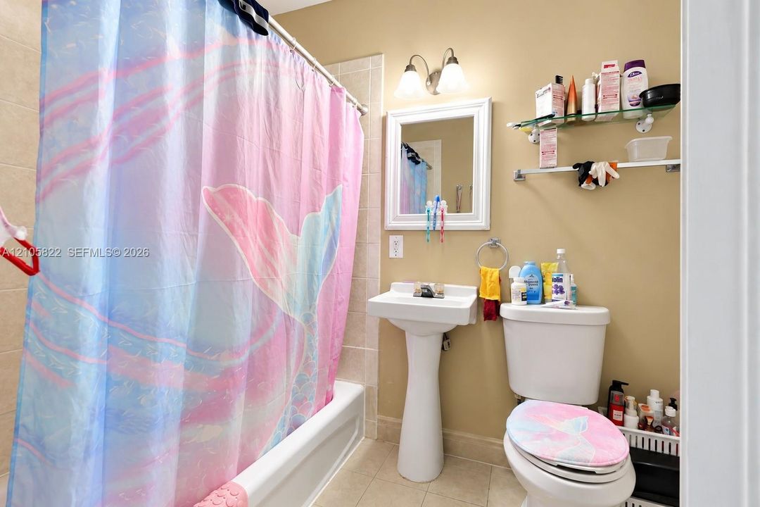 Bathroom featuring a white pedestal sink, a bathtub with tile surround, a wall-mounted glass shelf, and a dual-light fixture above a framed mirror