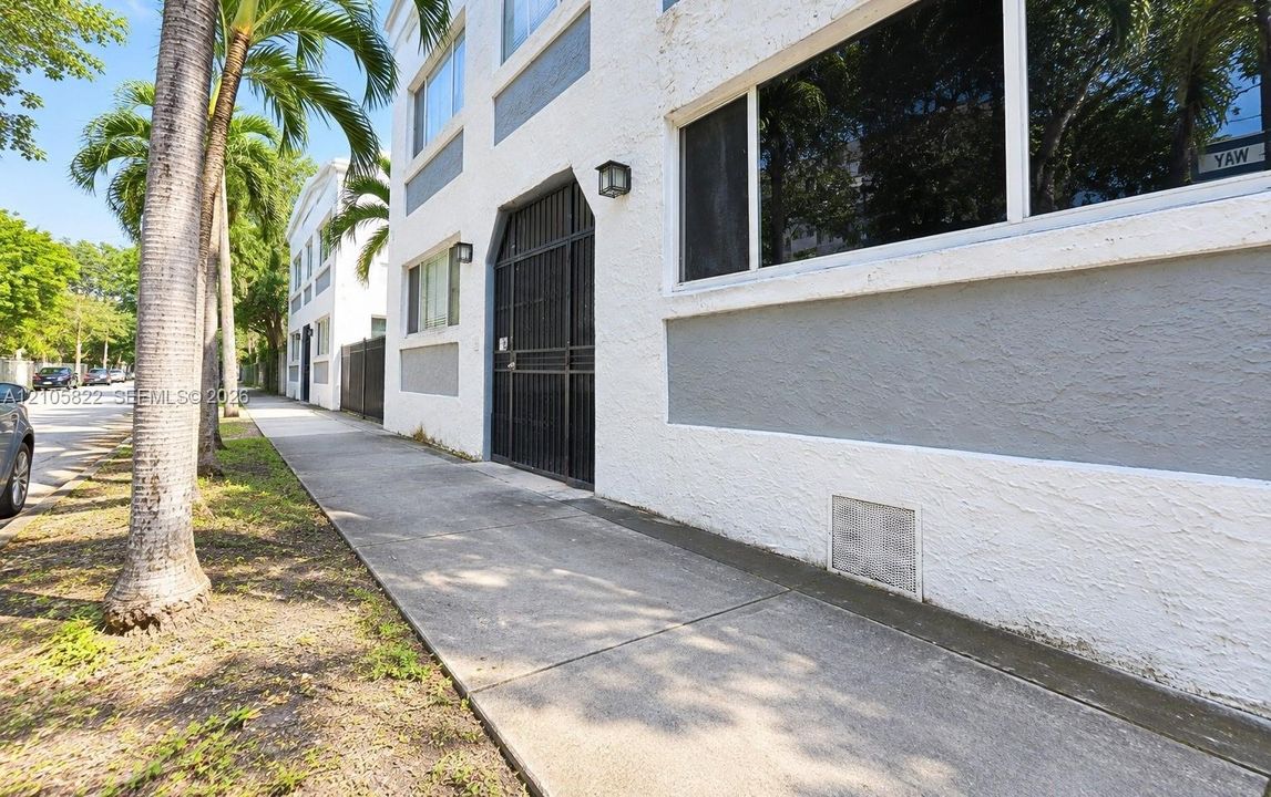Multi-story exterior featuring textured stucco facade, contrasting grey paneling, metal security gate, and large-pane windows