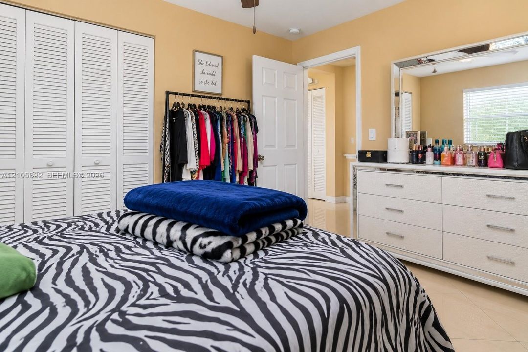 Bedroom featuring large-format tile flooring, ceiling fan, and white louvered-panel closet doors