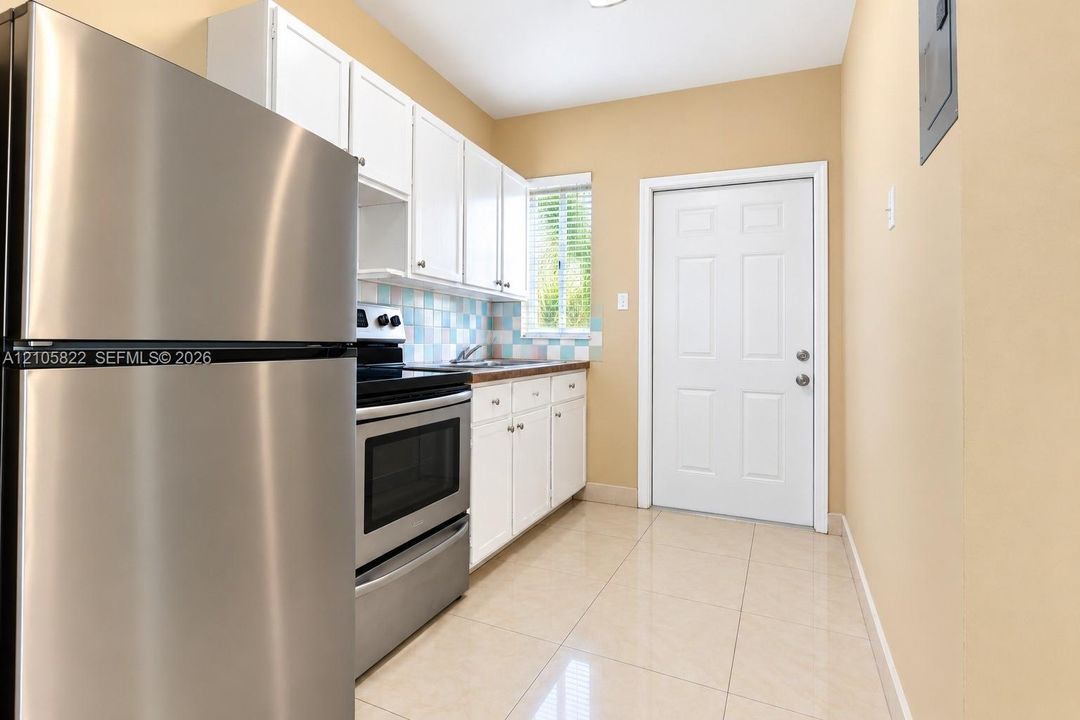 Kitchen featuring white shaker-style cabinetry, stainless steel refrigerator and range, multi-colored tile backsplash, and polished tile flooring