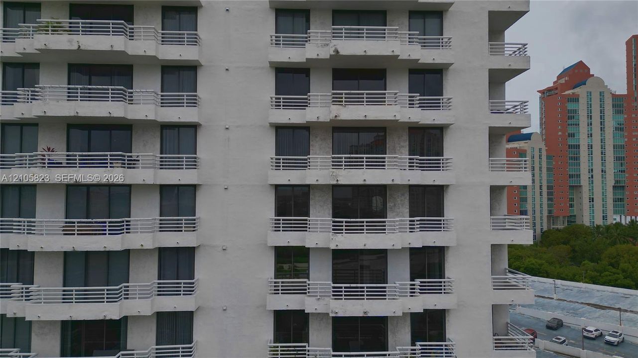 Multi-story residential facade featuring a grid of private balconies with horizontal railings and floor-to-ceiling glass sliding doors