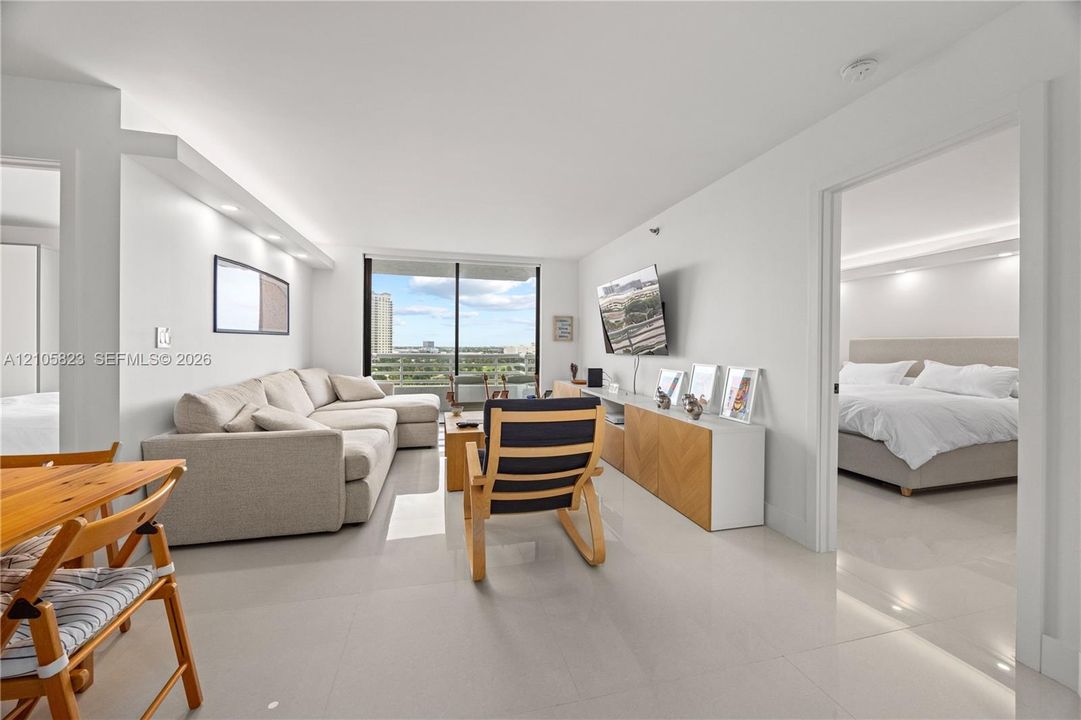 Open-concept living space featuring high-gloss tile flooring, recessed ceiling lighting, and floor-to-ceiling sliding glass doors leading to a balcony