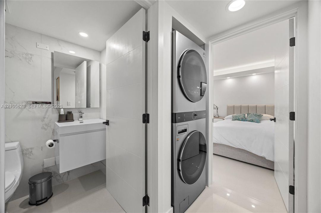 Stacked laundry unit featuring a metallic finish, wall-mounted floating vanity, rectangular vessel sink, and large-format tile wall cladding