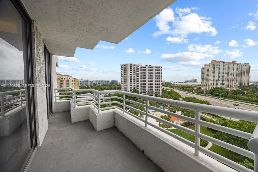 Covered balcony featuring white metal railings, concrete flooring, and sliding glass entry doors