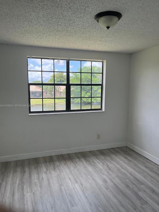 Neutral-toned interior space featuring light wood-finish flooring, a multi-pane window with a black frame, and a flush-mount ceiling light