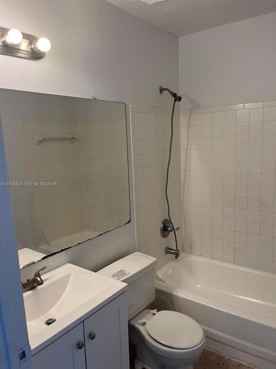 Bathroom featuring a white vanity cabinet with an integrated sink, rectangular wall-mounted mirror, two-light fixture, and a tile-surround shower and tub combination