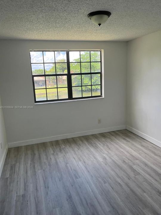 Room with wood-finish flooring, neutral wall paint, grid-pane window, and a flush-mount ceiling fixture