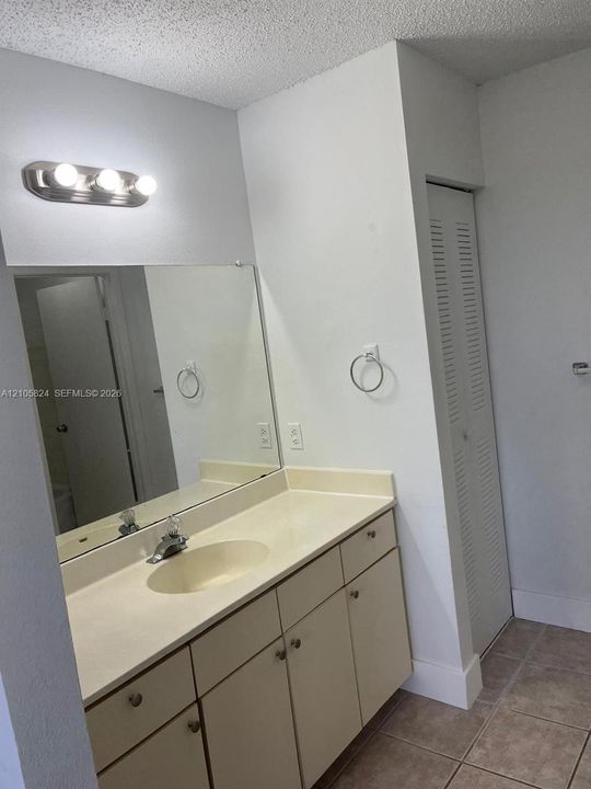 Single-vanity cabinet with an integrated countertop and basin, large-format vanity mirror, three-bulb wall-mounted lighting fixture, and tile flooring