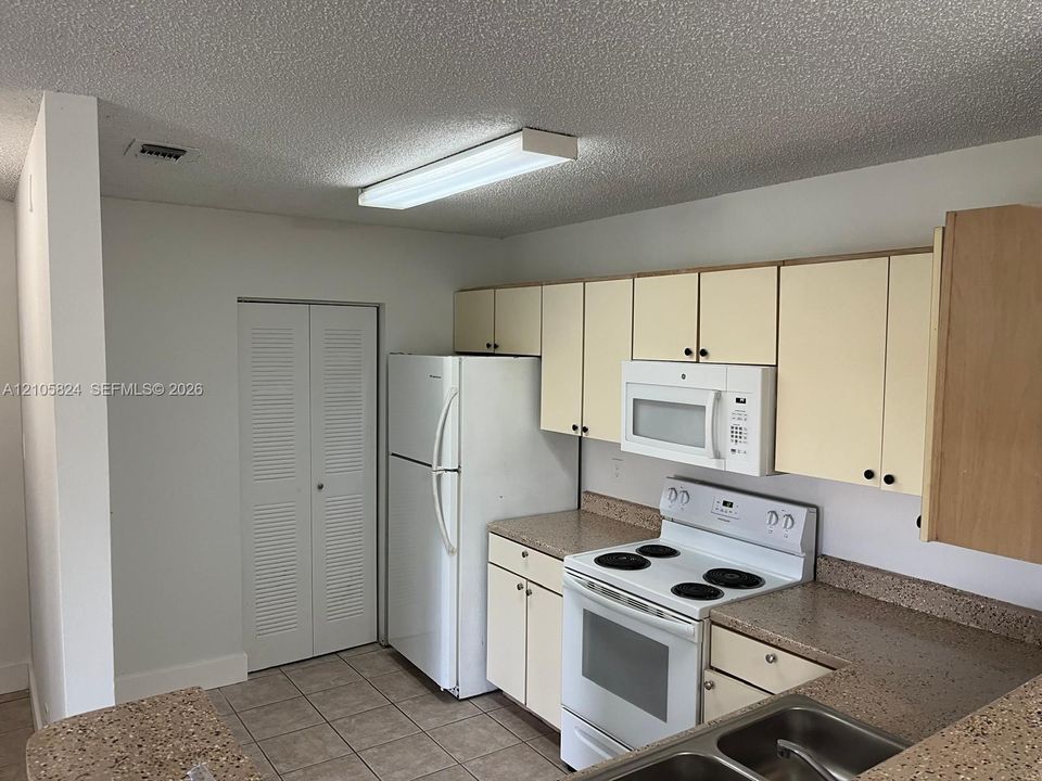 Kitchen featuring light-finish cabinetry, neutral solid-surface countertops, dual-basin stainless steel sink, and white appliances including an electric range and built-in microwave