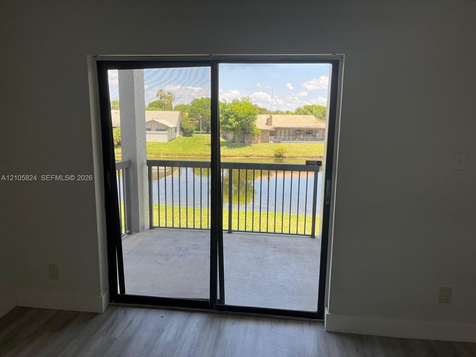 Sliding glass door opening to a covered balcony with metal railing, wood-finish flooring, and water frontage