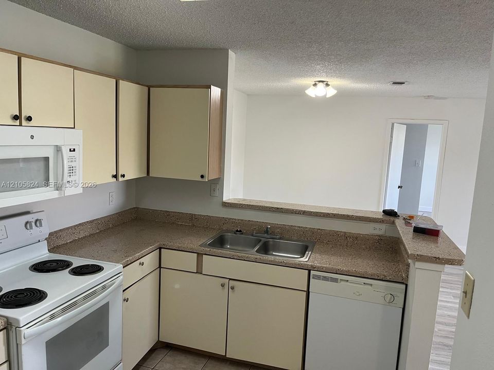 Kitchen featuring light-finish cabinetry, stone-texture laminate countertops, dual-basin stainless steel sink, and white appliances including a built-in microwave and dishwasher