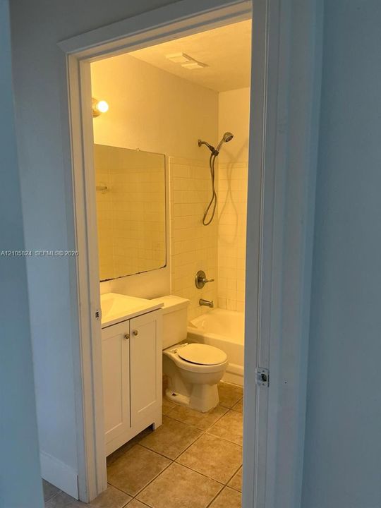 Bathroom featuring tile flooring, a white vanity cabinet, a wall-mounted mirror, a tub-shower combination with white subway-style wall tiling, and a handheld shower head