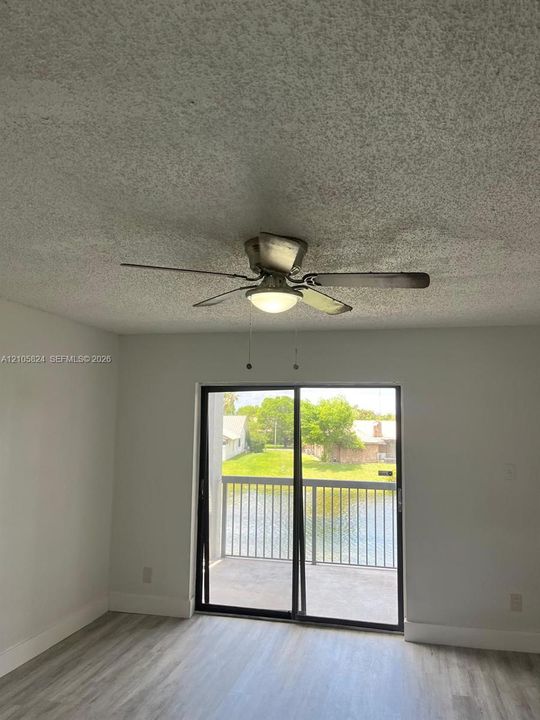 Wood-finish flooring, ceiling fan with integrated light fixture, and glass sliding door providing outdoor balcony access with waterfront scenery