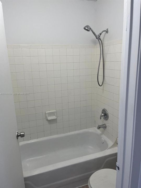 Bathtub enclosure featuring white square tile surround, chrome wall-mounted showerhead, and integrated soap dish