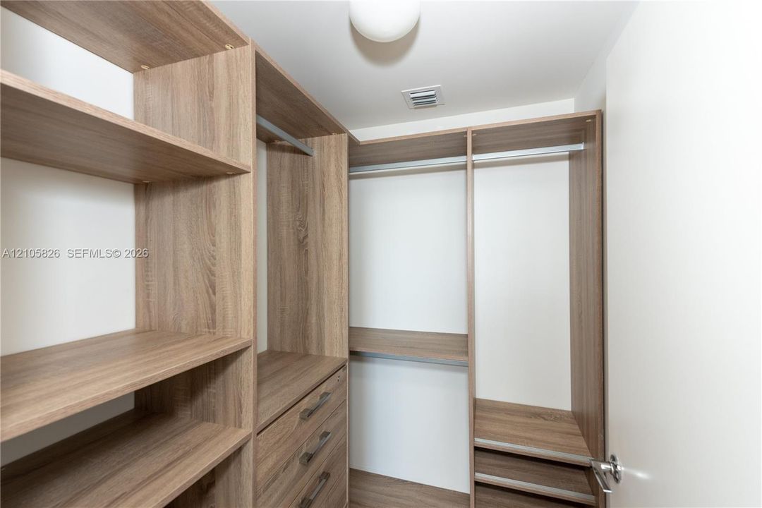 Custom walk-in closet featuring wood-finish shelving, integrated storage drawers with metal hardware, and metal hanging rods