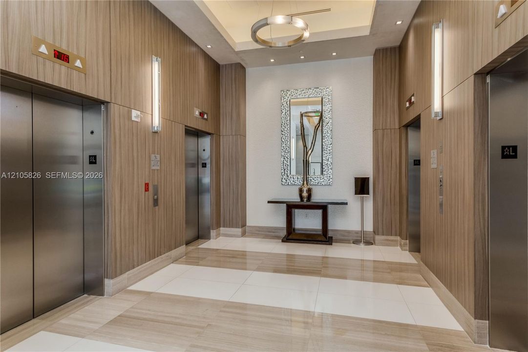 Elevator lobby featuring wood-panel wall cladding, large-format tile flooring, a circular pendant light fixture, and vertical wall-mounted lighting