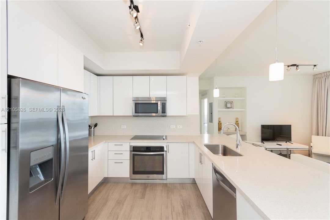 Modern kitchen featuring high-gloss white cabinetry, quartz countertops, stainless steel appliances, a peninsula breakfast bar, and wood-finish flooring