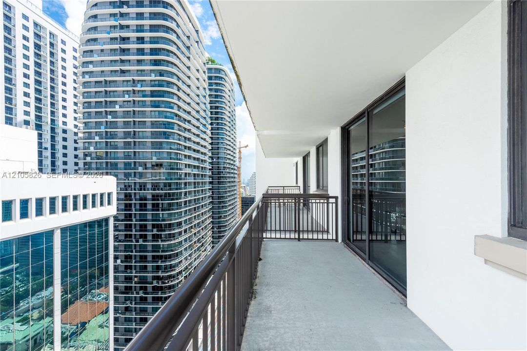 Covered balcony featuring metal railings and sliding glass door access