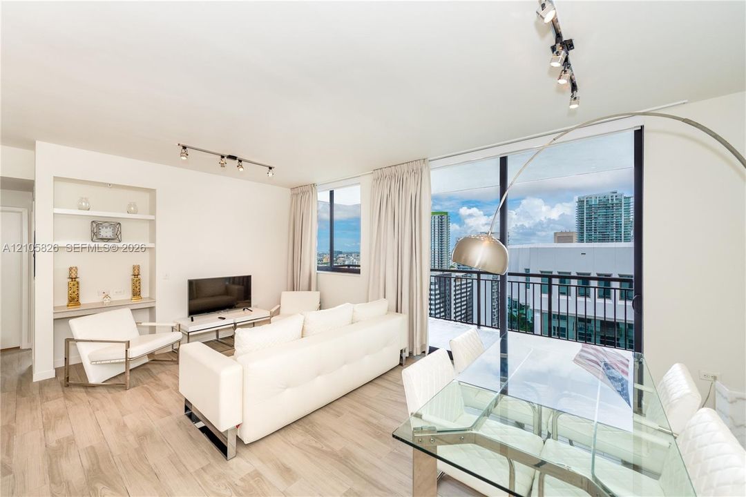 Open-concept living space featuring wood-finish flooring, floor-to-ceiling windows, a private balcony with metal railing, and built-in shelving with integrated counter space