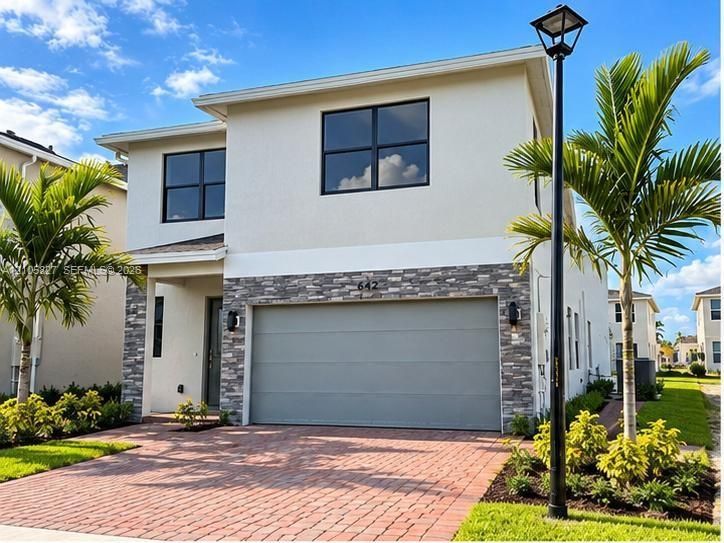 Two-story exterior featuring a light-toned stucco facade, stone veneer accents, a paver driveway, and a two-car garage