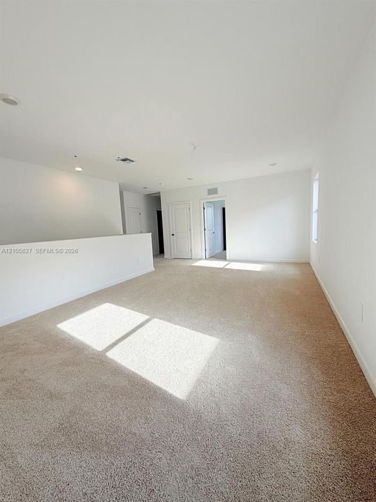 Expansive carpeted room featuring a half-wall partition, neutral wall tones, recessed lighting, and multi-panel interior doors