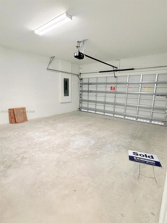 Garage space featuring a concrete floor, motorized sectional overhead door, ceiling-mounted fluorescent lighting, and an integrated electrical panel