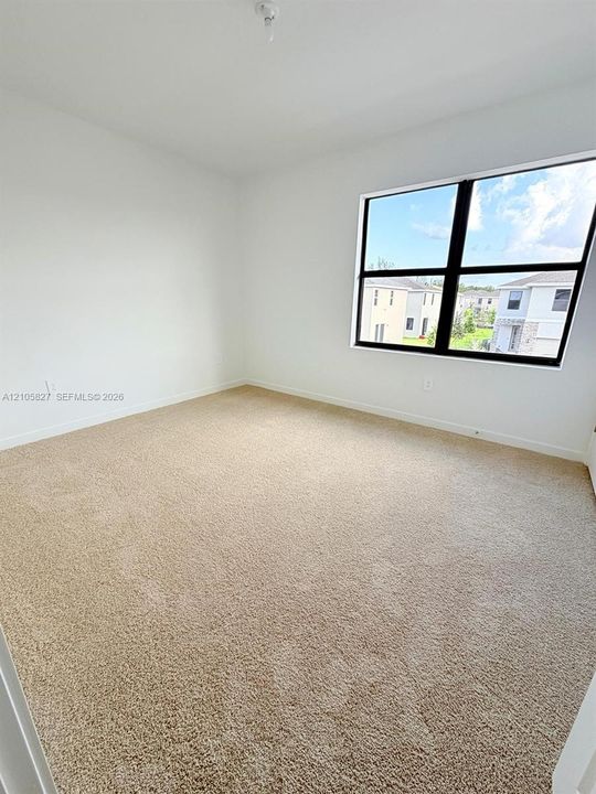 Neutral interior room featuring neutral carpeting, white walls, and a large black-framed window