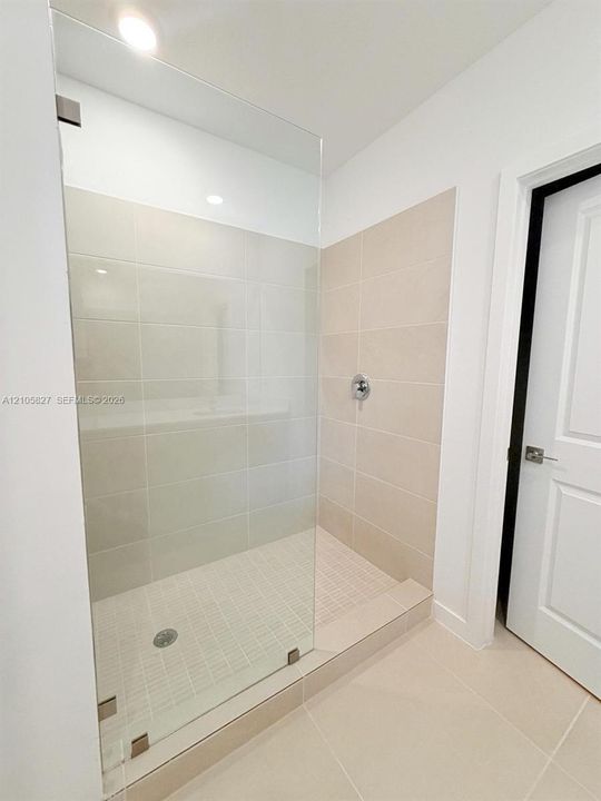Walk-in shower featuring a frameless glass enclosure, neutral large-format tile surround, recessed lighting, and polished chrome plumbing fixtures
