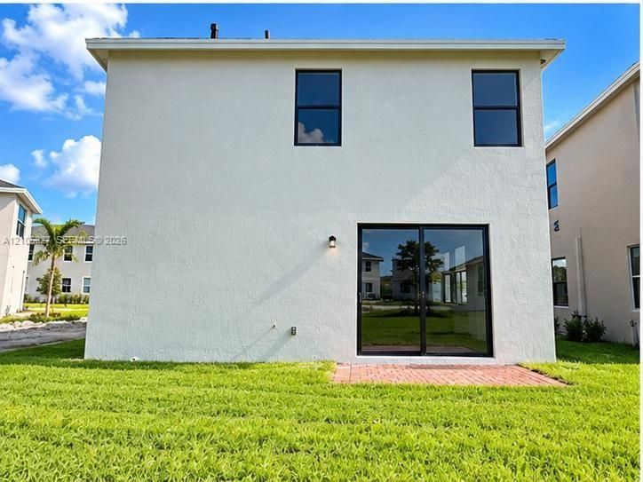 Two-story exterior with a smooth stucco finish, sliding glass door, brick paver patio, and black-framed windows