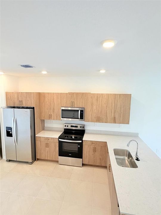 Kitchen featuring wood-finish cabinetry, light-toned countertops, stainless steel appliances, recessed ceiling lighting, and tile flooring