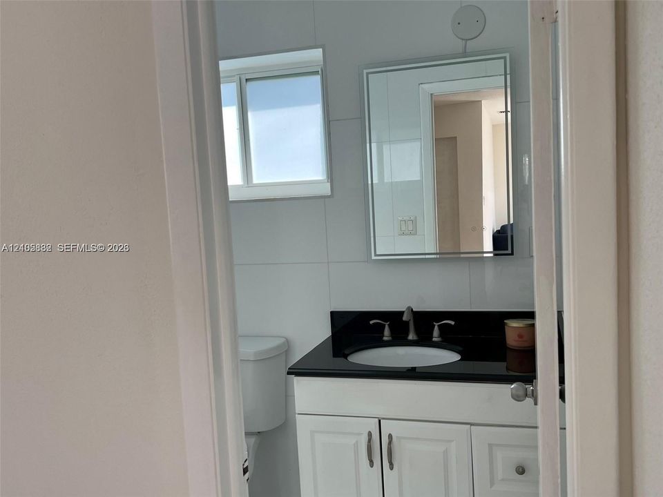 Bathroom featuring a white vanity cabinet, a dark countertop with an integrated oval basin, a rectangular mirror, and large-format wall tiling