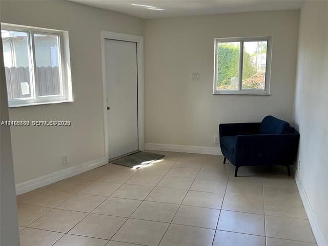 Neutral-toned interior space featuring large-format ceramic tile flooring, two sliding windows, and a solid-panel entry door