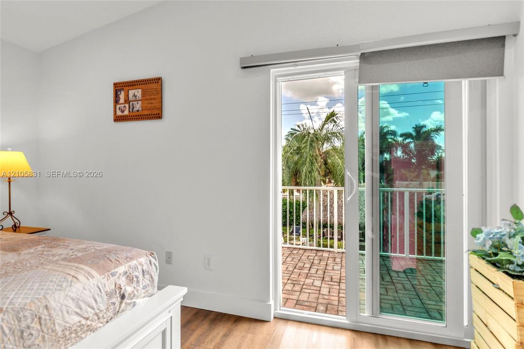 Sliding glass door with integrated roller shade, wood-finish flooring, and brick-paver balcony featuring a white metal railing