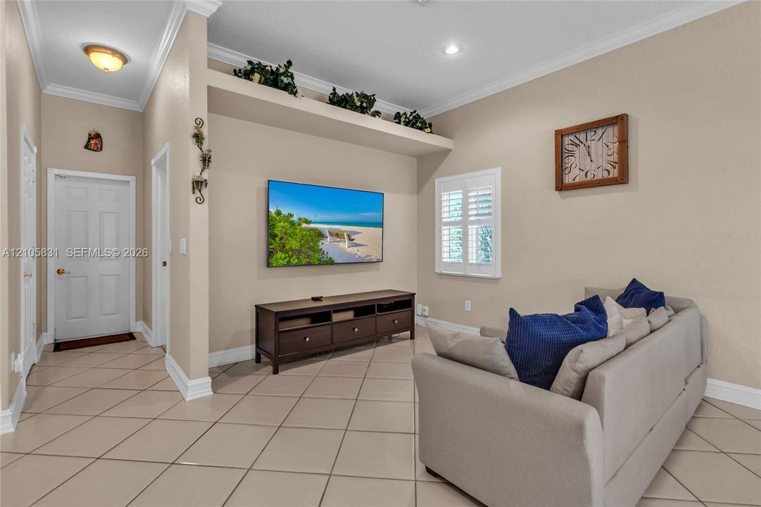 Interior space featuring large-format tile flooring, crown molding, built-in recessed display niche, and plantation shutters