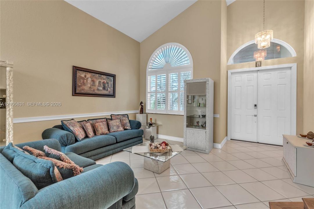 Vaulted ceilings featuring a chandelier, large arched window with custom shutters, transom window, and ceramic tile flooring