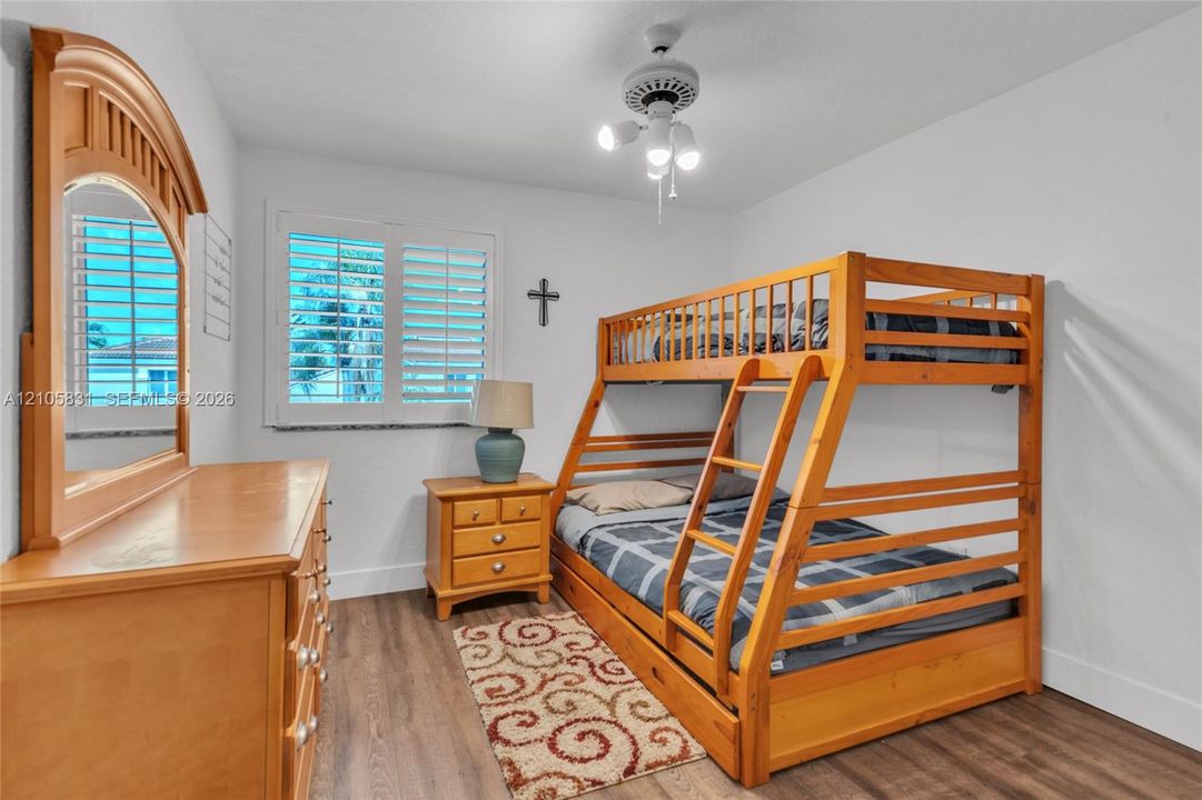 Interior room featuring wood-finish flooring, white plantation shutters, and a multi-light ceiling fan