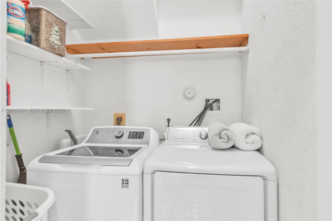 Laundry area featuring white top-loading washer and dryer, mounted wood-finish shelving, and wall-mounted plumbing hookups