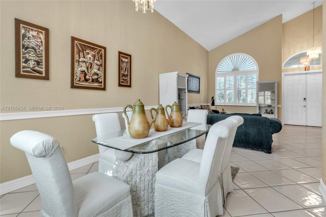 Vaulted ceilings, arched windows with plantation shutters, tile flooring, and chair rail molding