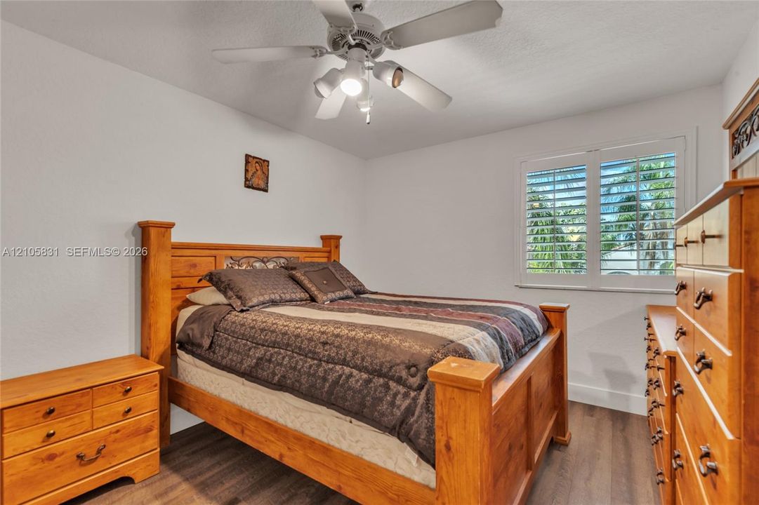 Wood-finish flooring, white plantation shutters, and a multi-light ceiling fan