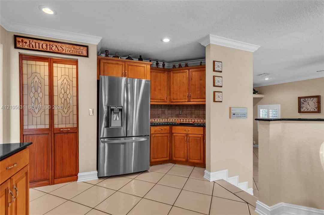 Kitchen featuring custom wood cabinetry, stainless steel French-door refrigerator, tile flooring, recessed lighting, and pantry doors with decorative glass inserts