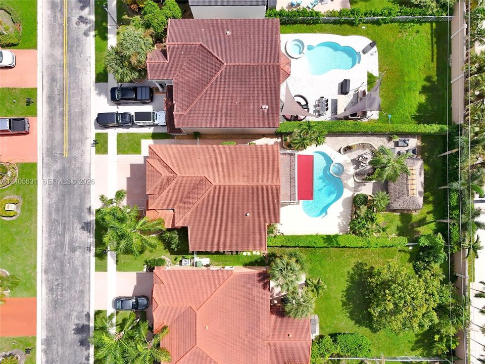 Aerial perspective of a residential property featuring an in-ground swimming pool with an integrated spa, a paved patio area, manicured landscaping, and a detached palapa