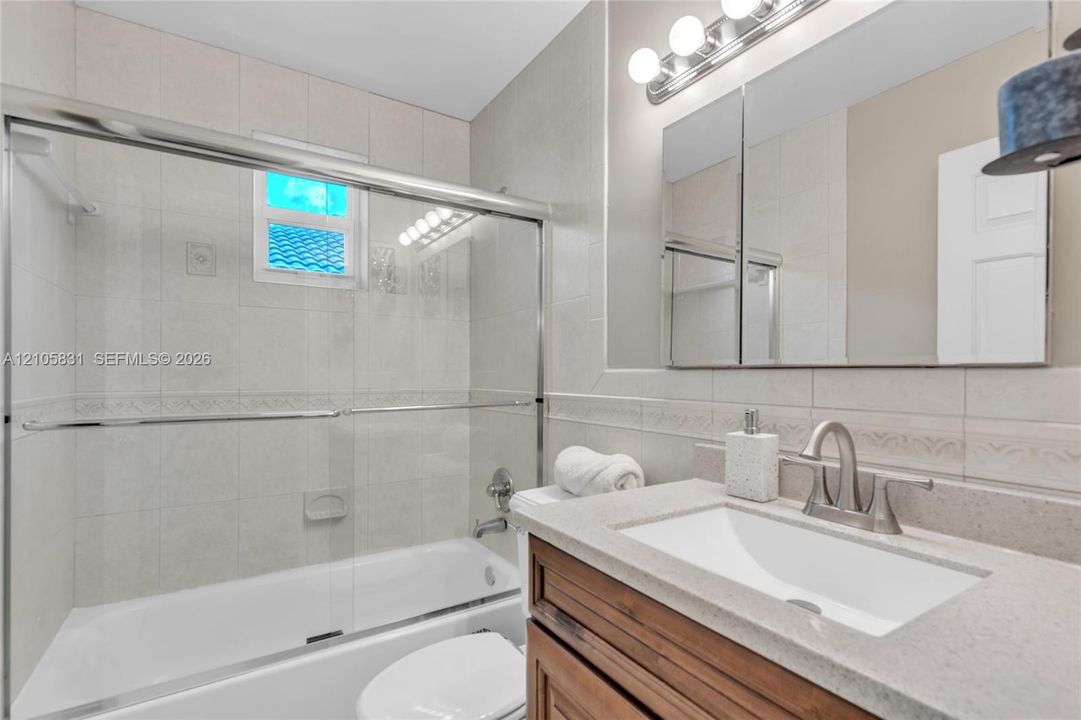 Bathroom featuring a vanity with stone-finish countertop and undermount sink, a tiled tub-shower combination with glass sliding doors, and a multi-bulb light fixture